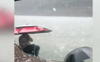 钓鱼人遇冰雹撑伞淡定垂钓：雨雹如蛋！